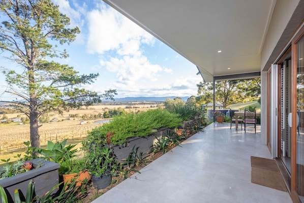 Enjoy a serene view of the vineyard and distant hills from this spacious balcony with a seating area and lush greenery.