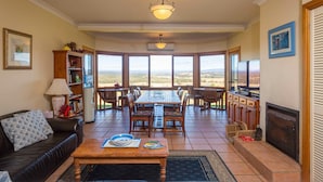 A spacious living room with a fireplace, a dining area, and large windows offering a view of the countryside.