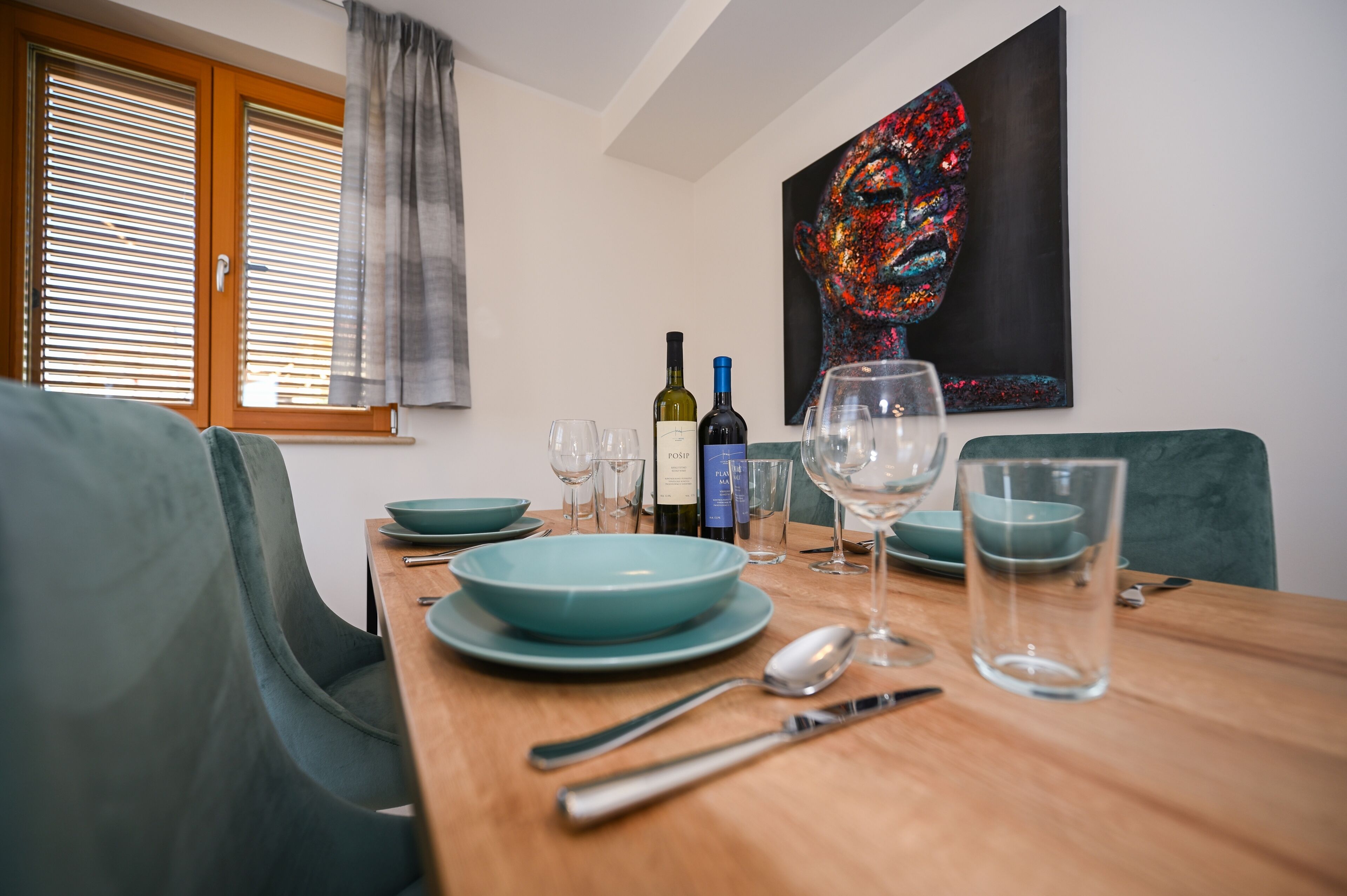 Uma área de jantar com uma mesa de madeira posta para dois, com pratos azul-turquesa, garrafas de vinho e copos.