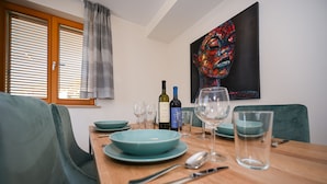 Comedor con una mesa de madera dispuesta para dos personas, con platos verde azulado, botellas de vino y copas.