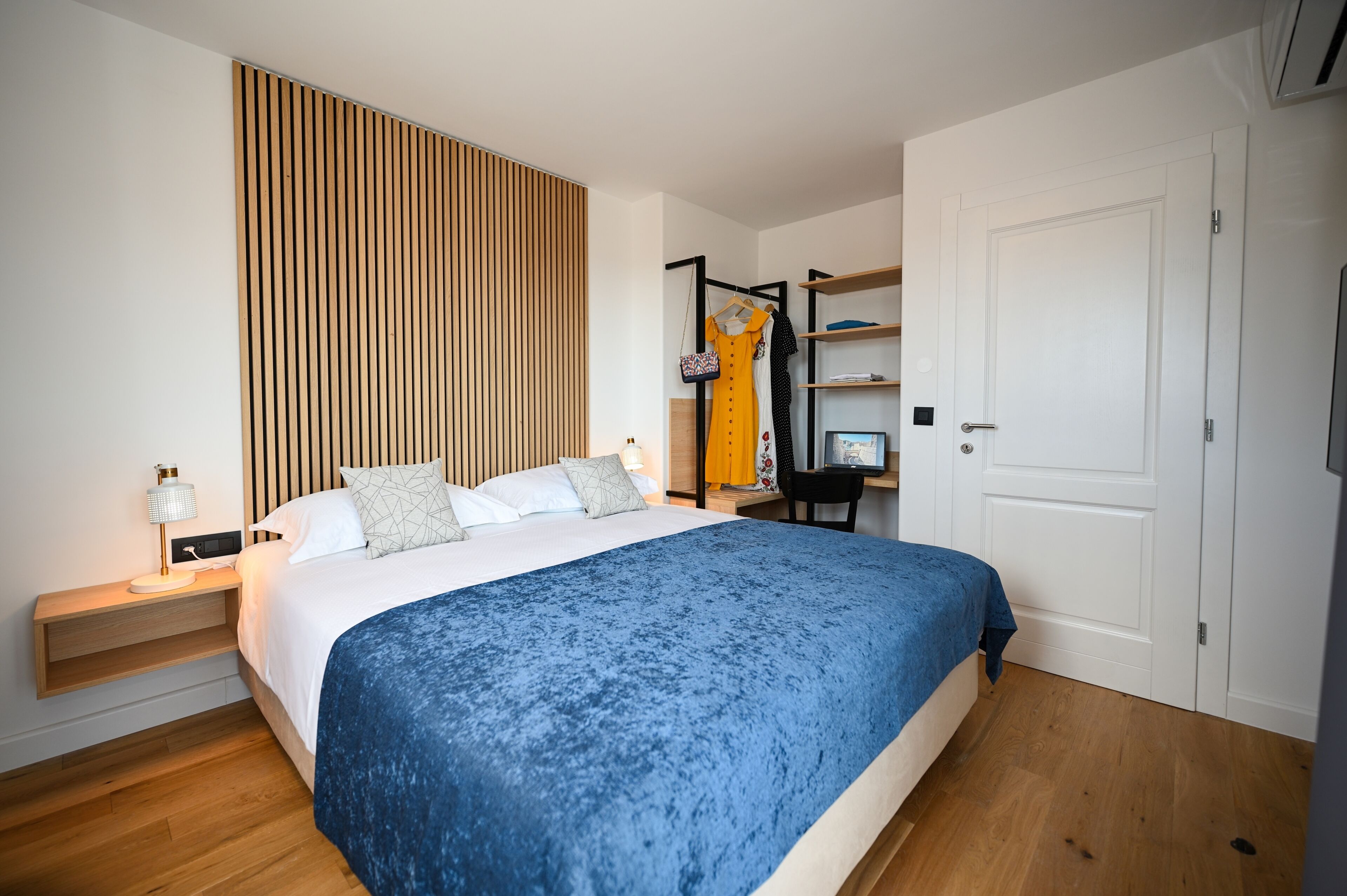 A modern bedroom with a large bed, a wooden slat wall, a wardrobe, and a desk with a chair.