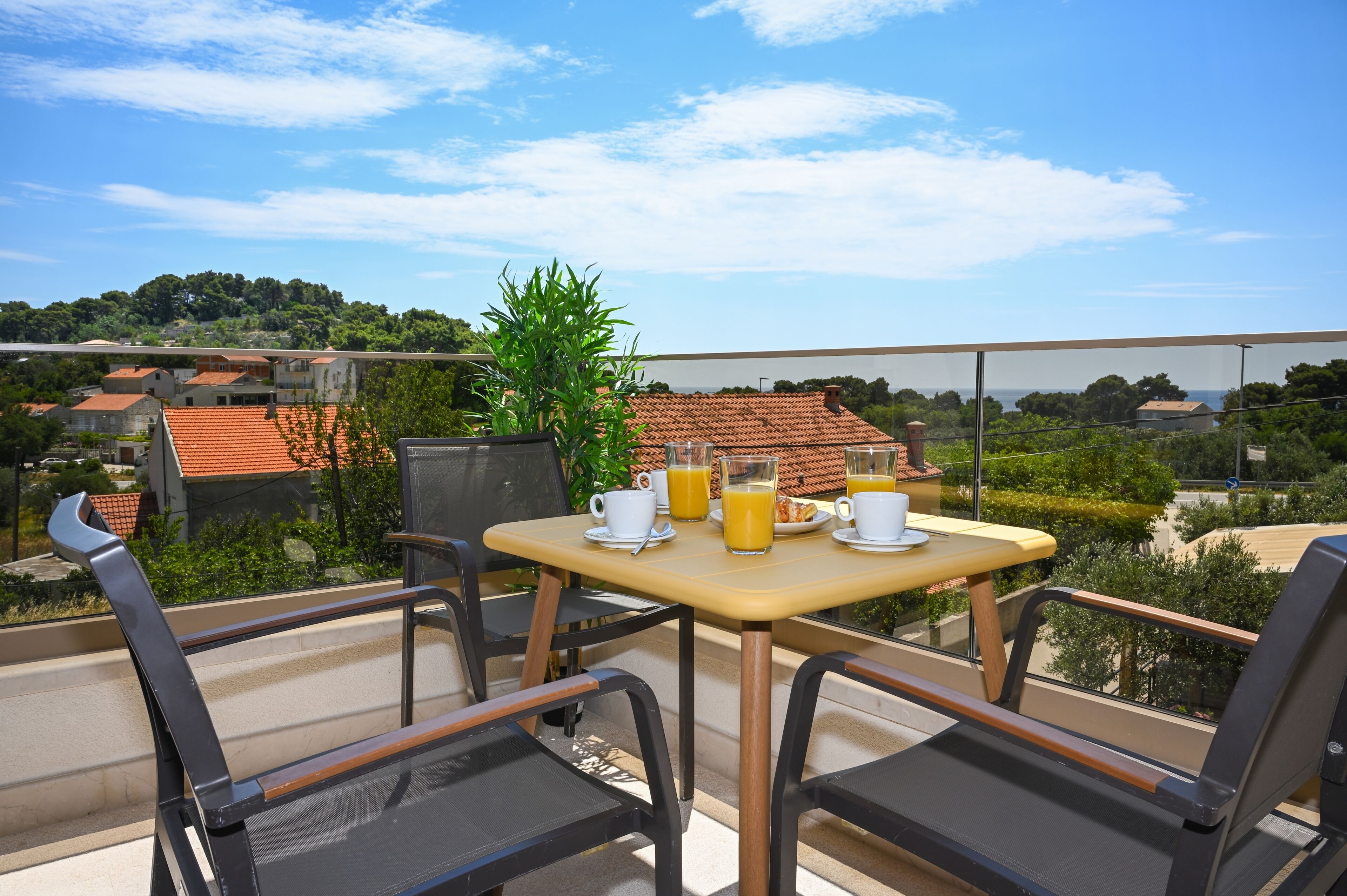 A balcony with a table set for breakfast, overlooking a residential area with red-tiled roofs.