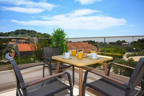 Un balcón con una mesa preparada para el desayuno, con vistas a una zona residencial de tejados rojos.