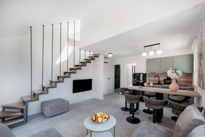 A modern living space with a staircase, a flat-screen TV, a dining area with bar stools, and a kitchen with a large mirror. - Casa Laurea (Dubrovnik)