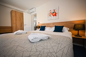 A hotel room with a large bed, a wooden wardrobe, a painting on the wall, and a nightstand with a lamp. - Casa Laurea (Dubrovnik)