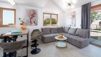 A modern living room with a sectional sofa, a dining table with chairs, a small round table with a bowl of fruit, and artwork on the walls.
