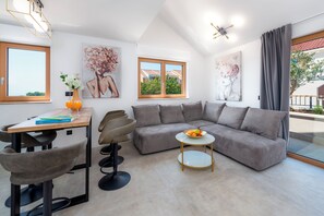 A modern living room with a sectional sofa, a dining table with chairs, a small round table with a bowl of fruit, and artwork on the walls.
