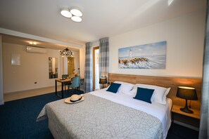A hotel room with a large bed, a desk, a chair, a painting, and a chandelier. - Casa Laurea (Dubrovnik)