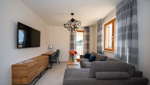 A modern living room with a sofa, a coffee table, a TV mounted on the wall, and a window with curtains. - Casa Laurea (Dubrovnik)