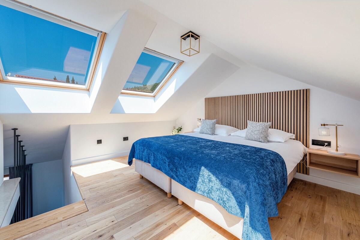 A modern bedroom with skylights, a wooden headboard, and a bedside table with a lamp.