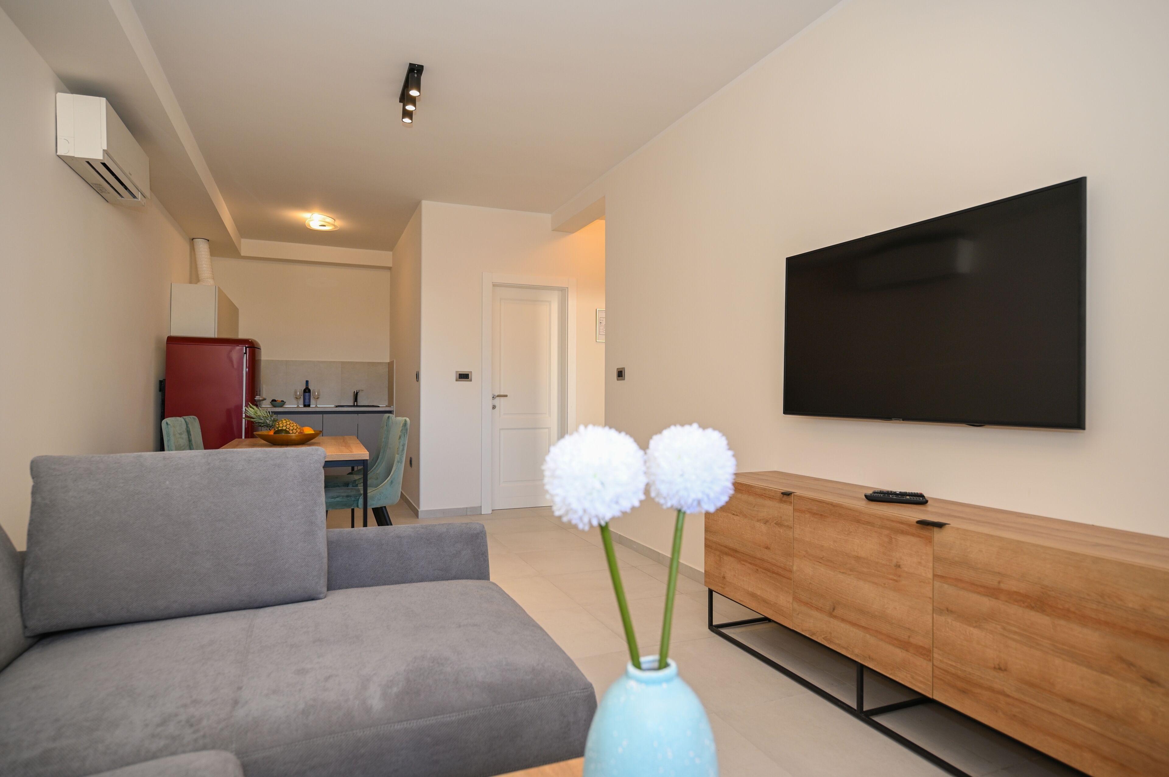 A modern living room with a grey sofa, a wooden TV stand, and a flat-screen TV mounted on the wall.
