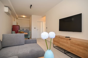 A modern living room with a grey sofa, a wooden TV stand, and a flat-screen TV mounted on the wall. - Casa Laurea (Dubrovnik)