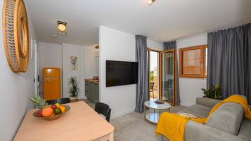 A modern living room with a flat-screen TV, a dining area with a fruit bowl, and a sofa with a yellow throw.