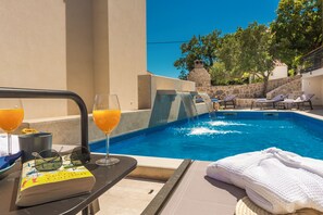 A poolside setting with a book, glasses, and drinks on a table, a towel, and lounge chairs. - Casa Laurea (Dubrovnik)