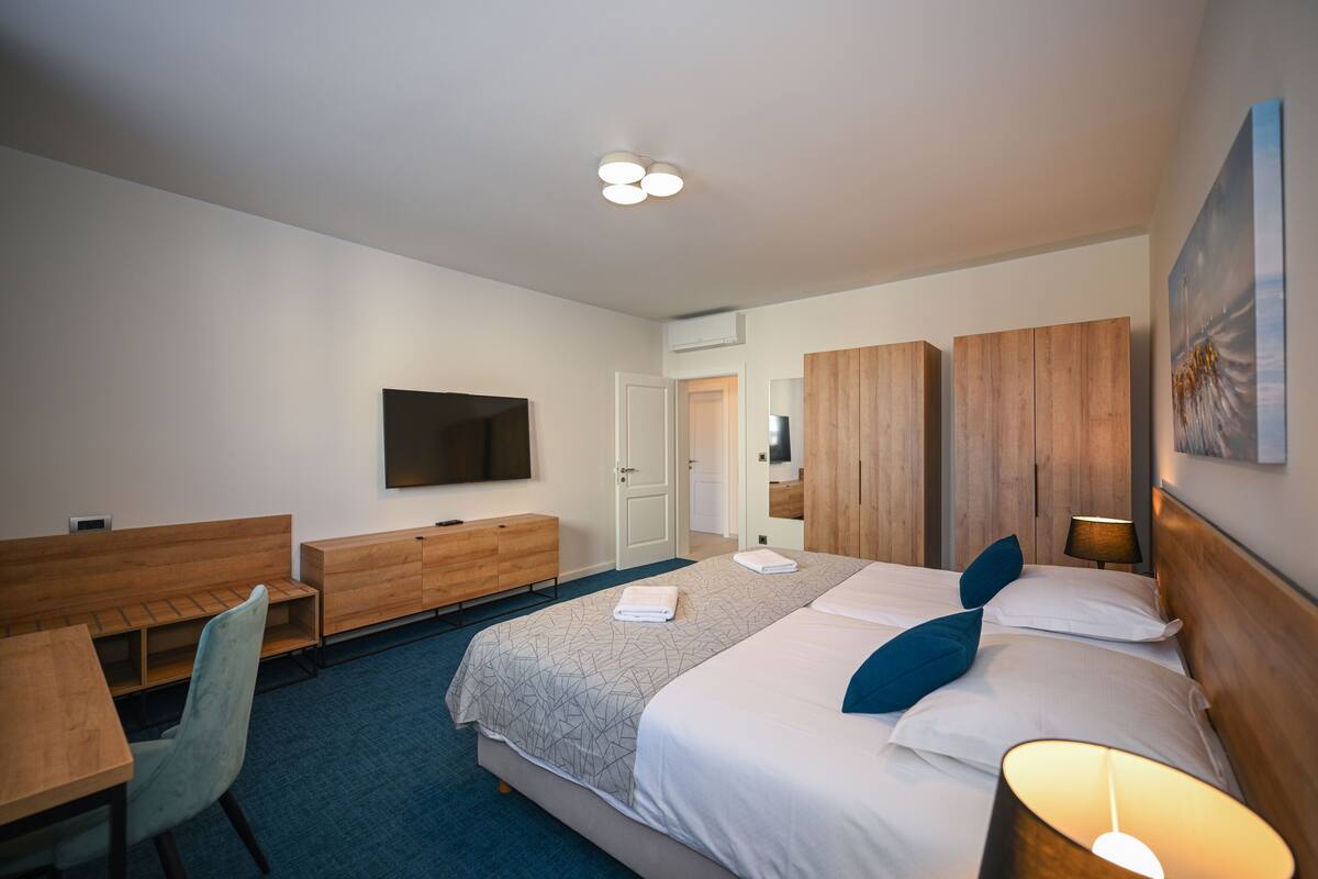A hotel room with a bed, a desk, a chair, a TV, wooden cabinets, and a painting on the wall.