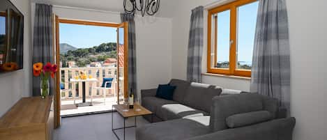 A modern living room with a grey sofa, a wooden table, and a view of the sea through a large window.