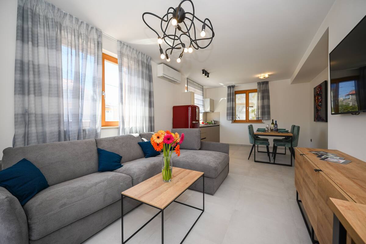 A modern living room with a grey sofa, a wooden coffee table, and a dining area with a wooden table and chairs.