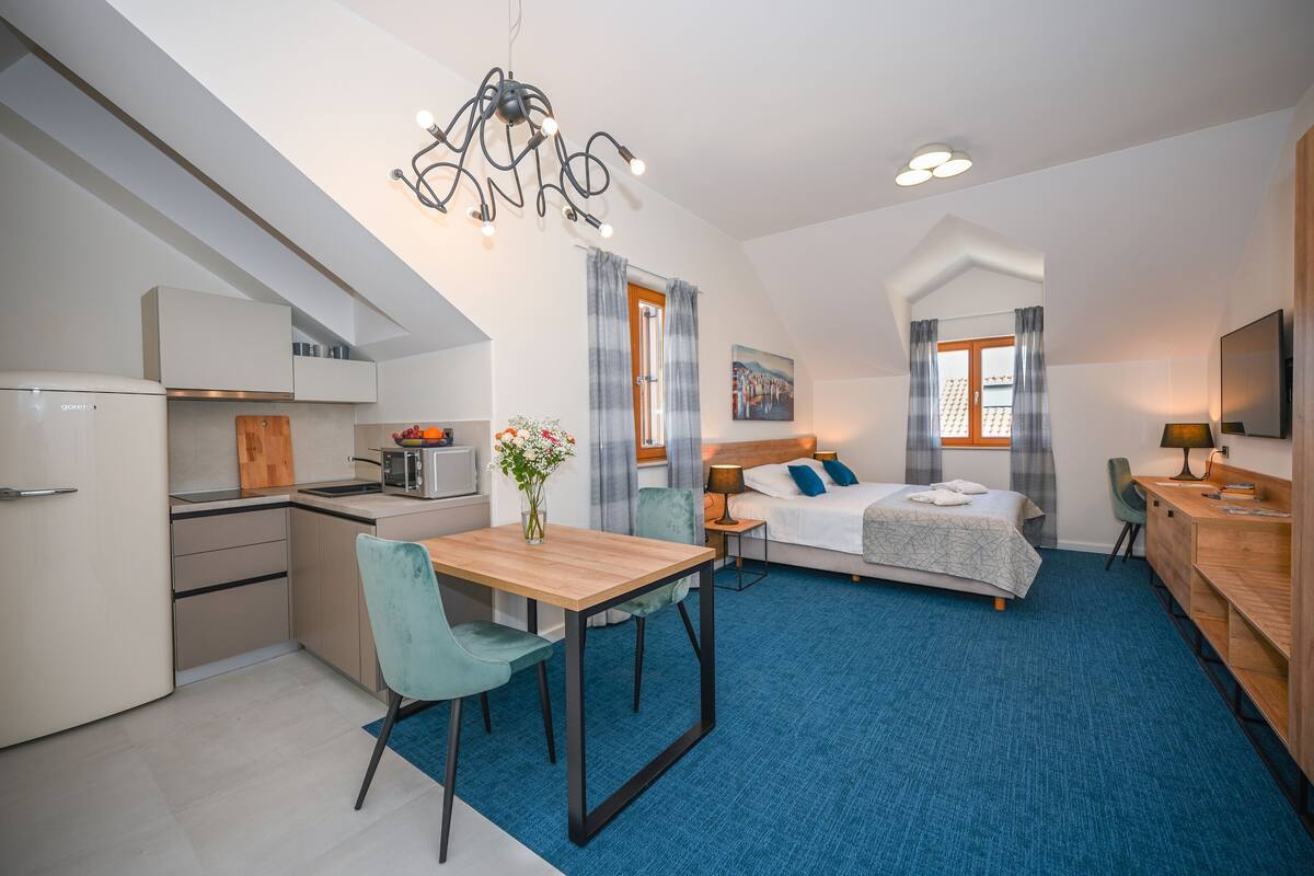 A modern hotel room with a kitchenette, a dining area, a bed, and a desk.