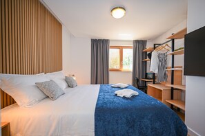 A hotel room with a bed, a wardrobe, a desk, and a window with curtains.