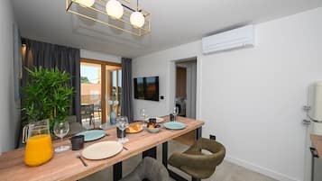 A modern dining area with a wooden table, chairs, a potted plant, and a television mounted on the wall.