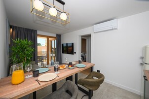 Uma sala de jantar moderna com uma mesa de madeira, cadeiras, uma planta em vaso e uma televisão fixada na parede.