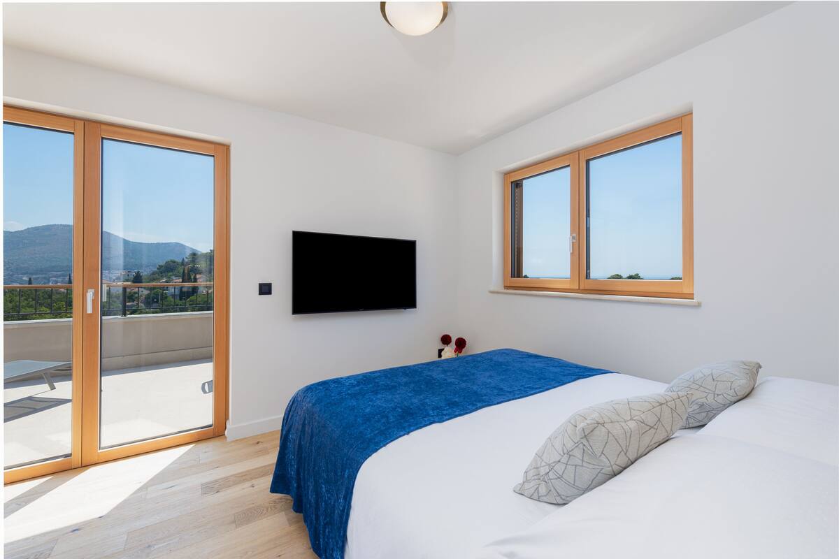 A bedroom with a bed, a TV, and a balcony with a view of the city and mountains.