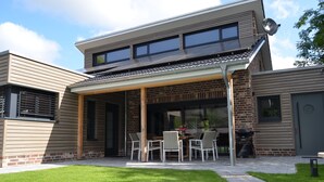 A modern two-story house with a covered patio, a brick exterior, and a satellite dish. - Tasteful vacation loft for 6 people in Emsland with sauna and outdoor pool (Emsbüren)
