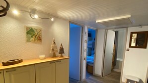 Un pasillo con piso de madera, una puerta blanca que da a un dormitorio y un taburete pequeño cerca de la puerta.