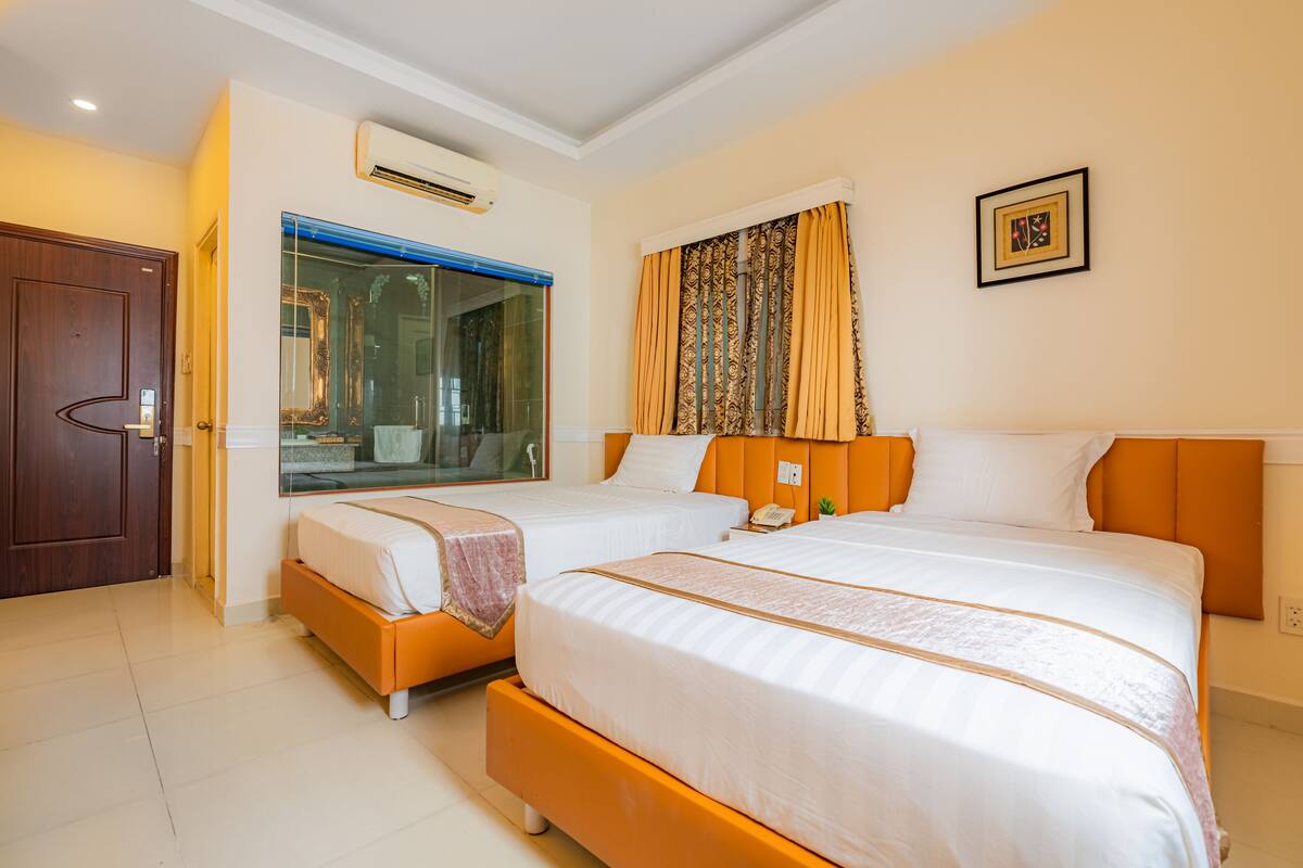 A hotel room with two beds, a large window with curtains, an air conditioning unit, and a framed picture on the wall.