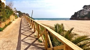 A wooden boardwalk leading to a beach with a rocky cliff in the background.