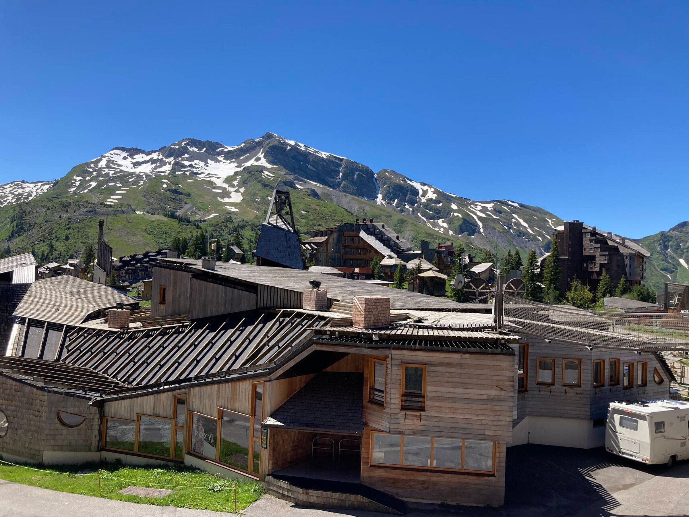 A rustic building with a sloped roof and large windows, surrounded by a mountainous landscape.