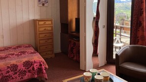 Un dormitorio con cama, cómoda de madera, televisor y balcón con vista a la ciudad.