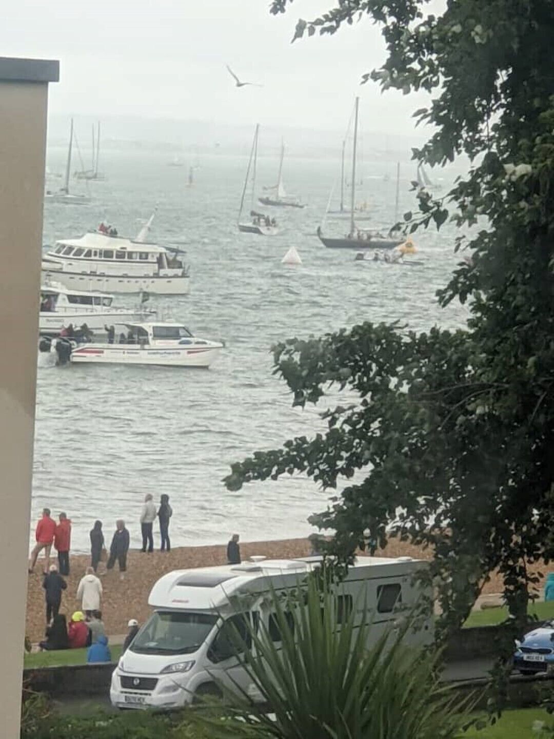 Ein Yachthafen mit Booten, einem weißen Transporter und Personen in der Nähe des Ufers.