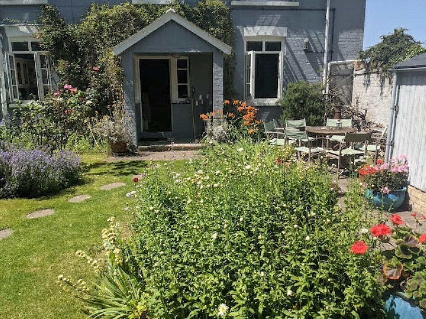 A residential garden with a small shed, a lawn, and various plants and flowers.