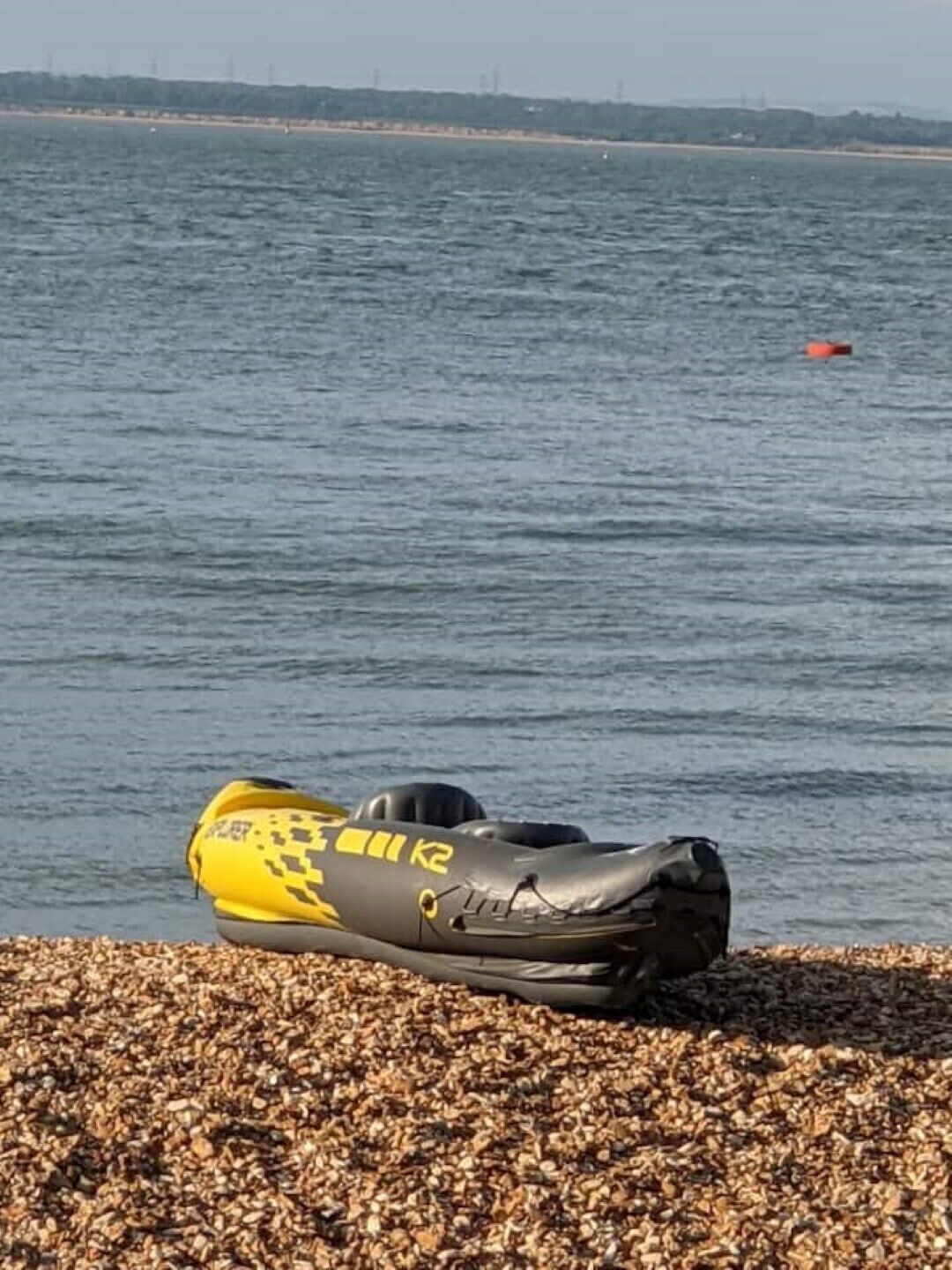 A kayak on a pebbled shore by a body of water.
