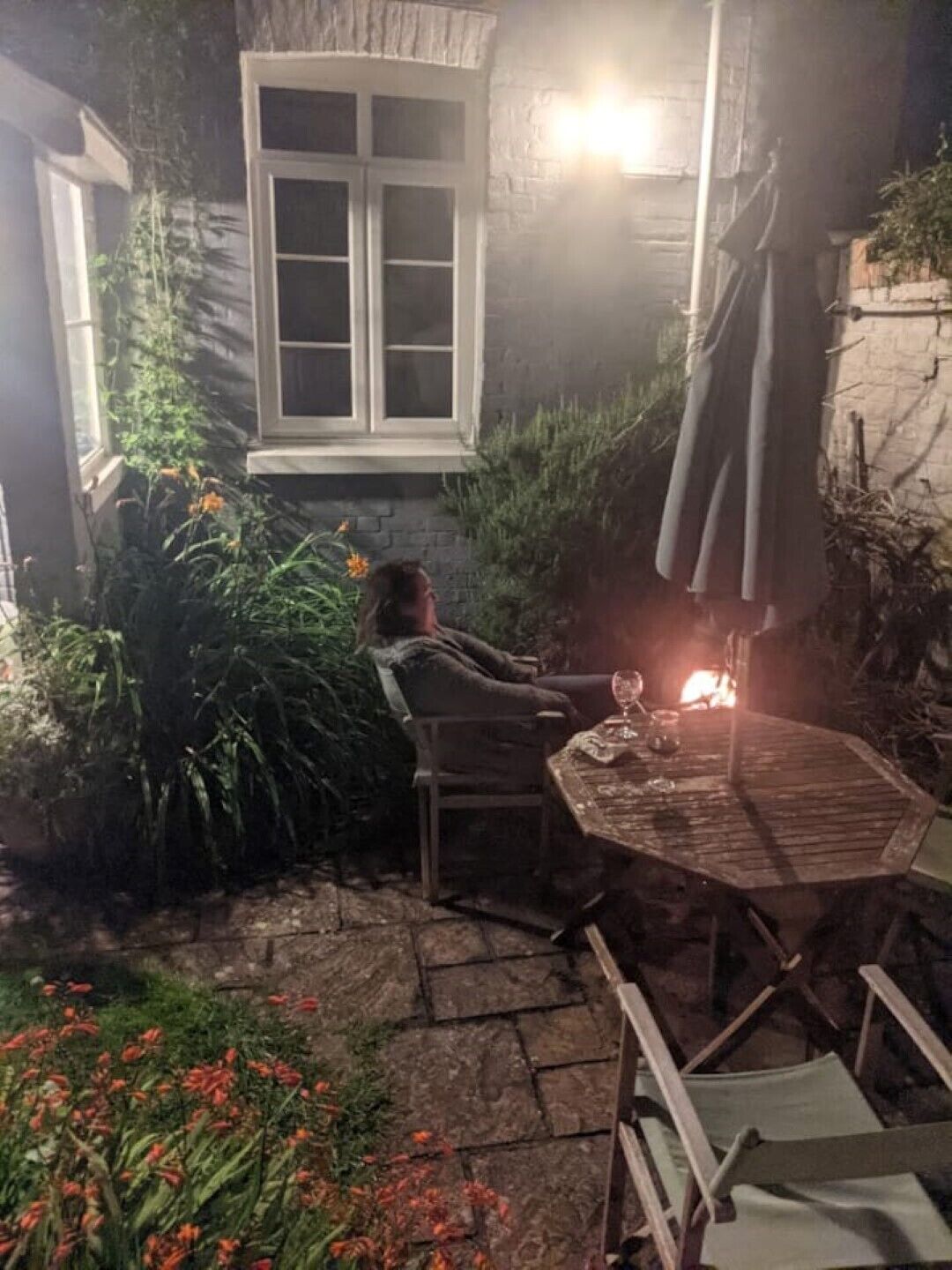 A cozy outdoor seating area with a table and chairs, surrounded by plants and a fire.