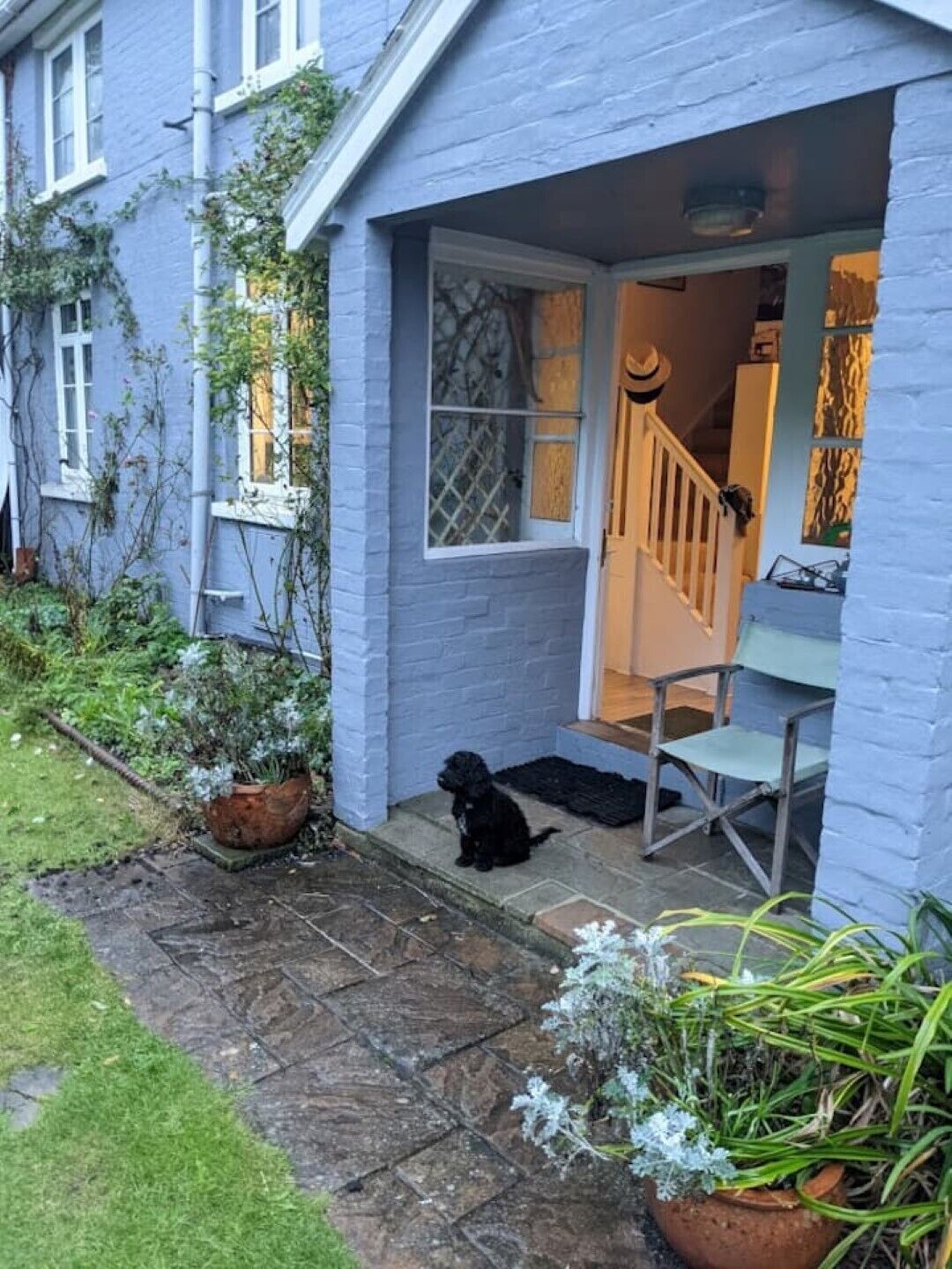 Une maison à l’extérieur bleue, avec un porche où se trouve un chien et un escalier menant à l’intérieur.