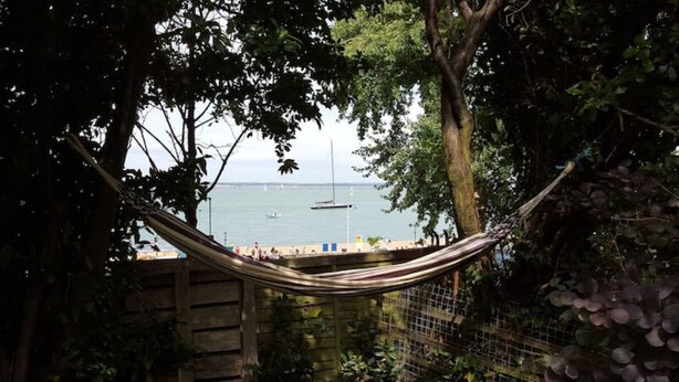 A hammock between trees overlooking a beach with boats and a fence. - Cliffside Cosy Cottage by Cowes Beach: 1x KING-Size Double BR & a Twin/Kids BR (Cowes)