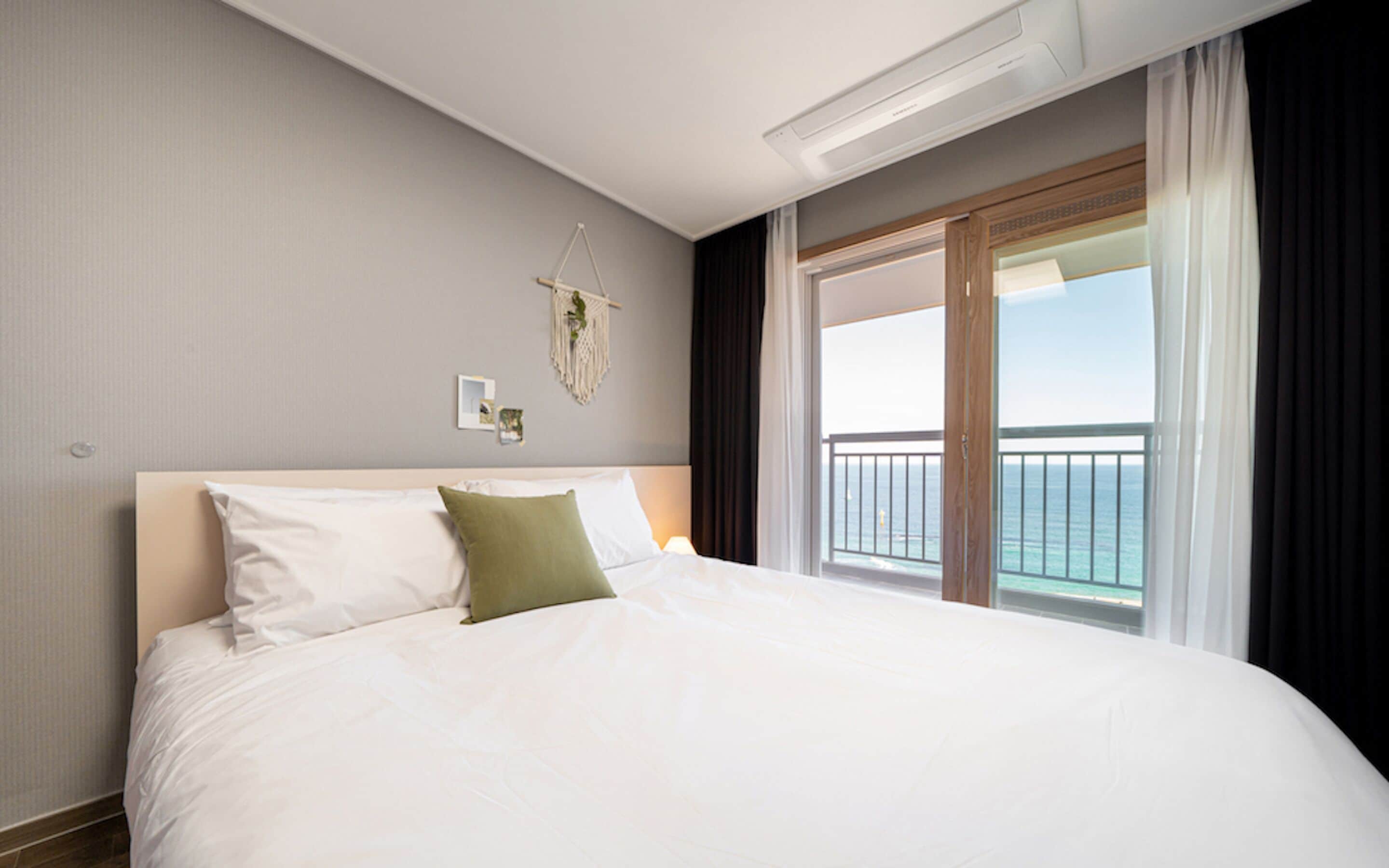 Una habitación de hotel con una cama grande, vista al océano desde un balcón y un tapiz de macramé en la pared.