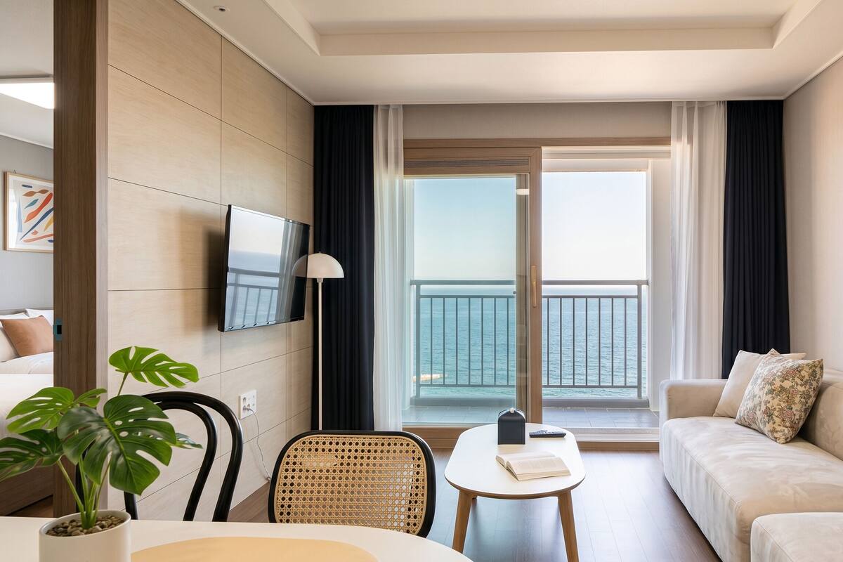 Ein Hotelzimmer mit Balkon, einem an der Wand montierten Fernseher, einer Couch, einem Esstisch und einem Stuhl.