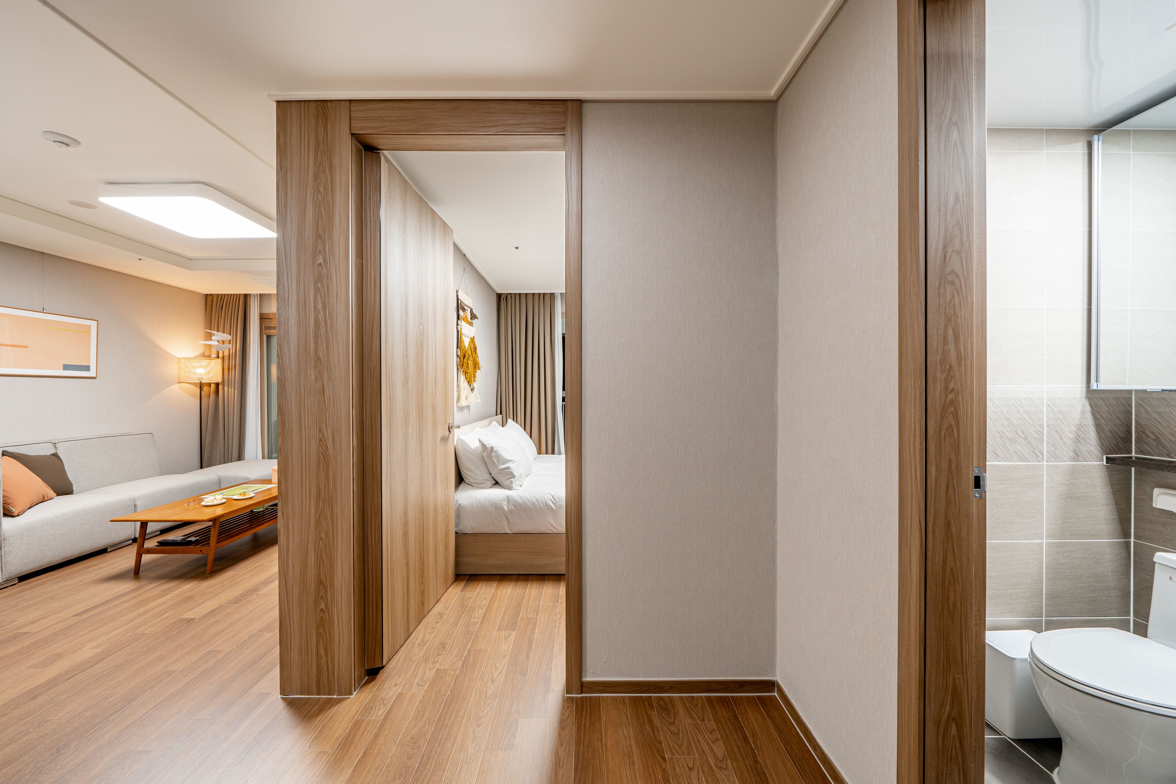 Una habitación de hotel moderna con piso de madera, una cama con sábanas blancas, un sofá y una pequeña mesa.