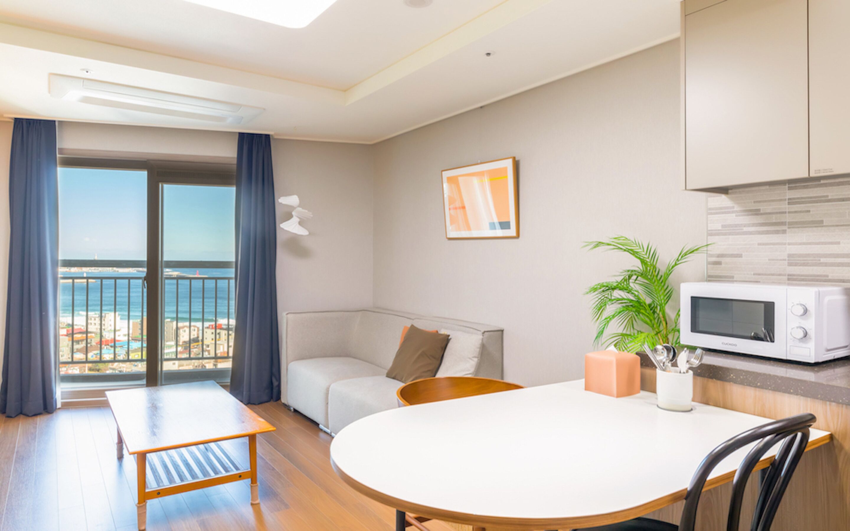 A modern living room with a balcony, a dining table, a sofa, and a kitchen area with a microwave.