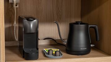 A kitchen area with a coffee maker, a kettle, and a coffee grinder on a wooden countertop.
