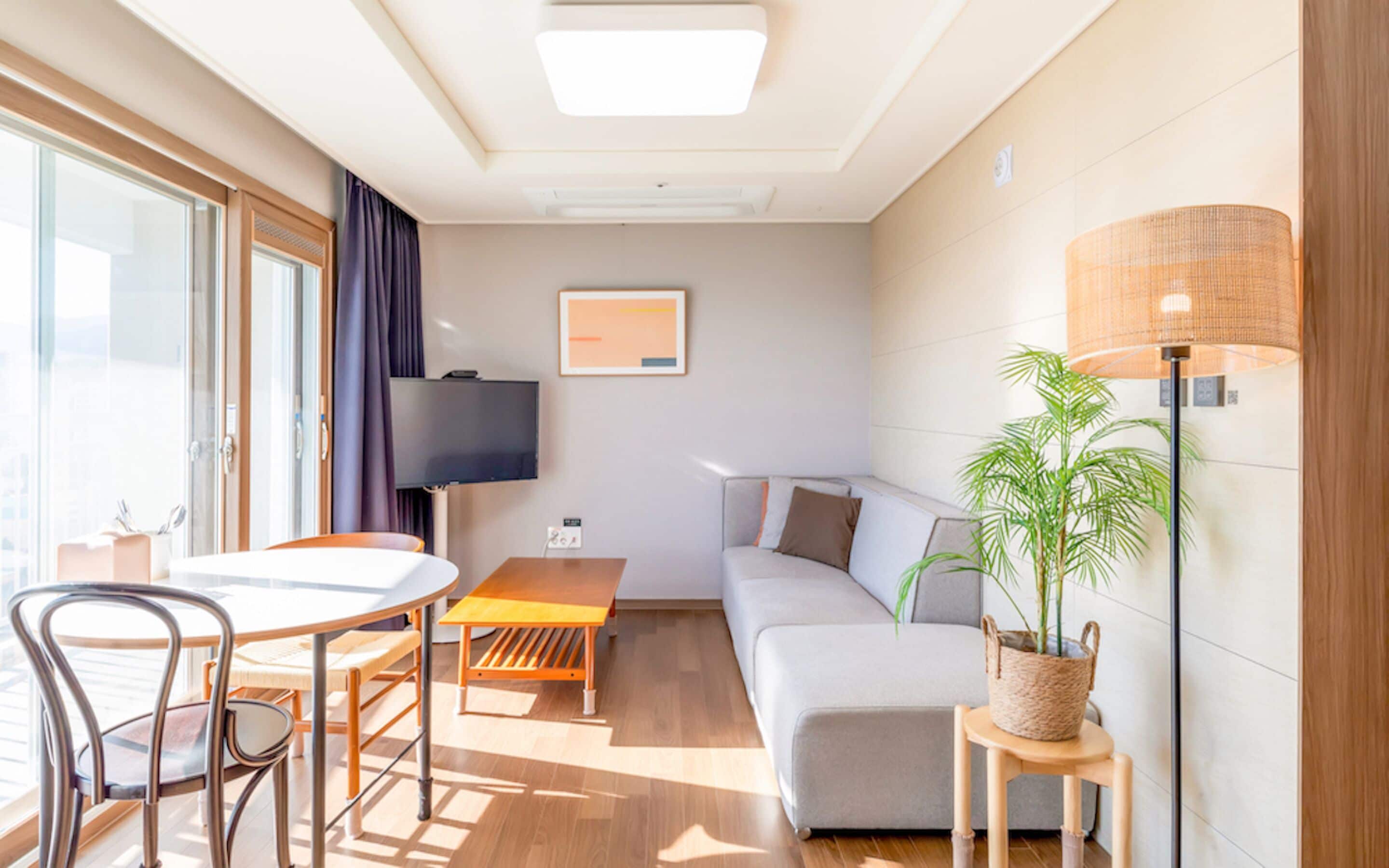 A modern room with a dining table, chairs, a sofa, a TV, and a lamp.