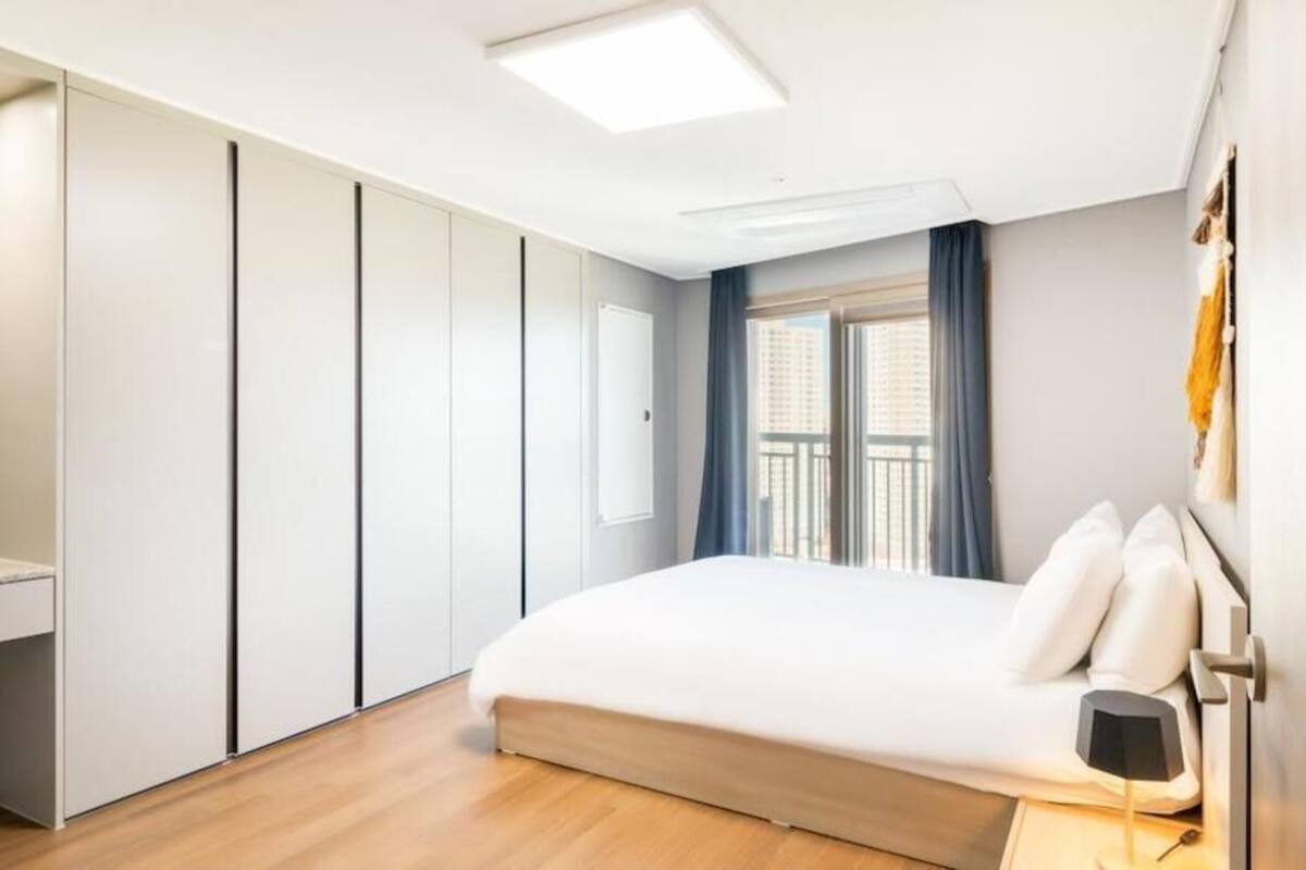 Ein Schlafzimmer mit Bett, Nachttisch, Lampe, Kleiderschrank und einem Fenster mit Vorhängen.