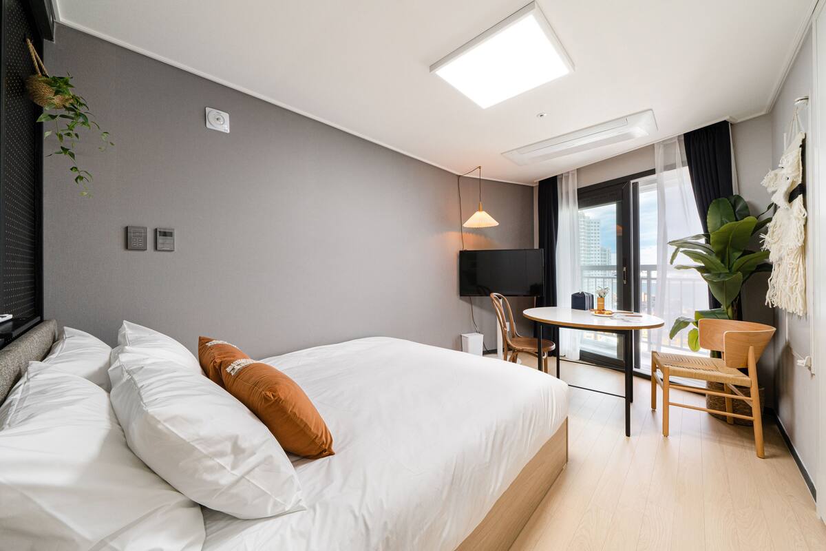 Ein Hotelzimmer mit Bett, Nachttisch, Sessel, Fernseher und Blick auf die Stadt.