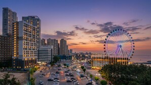 A cityscape with modern high-rise buildings, a large Ferris wheel, and a busy street.