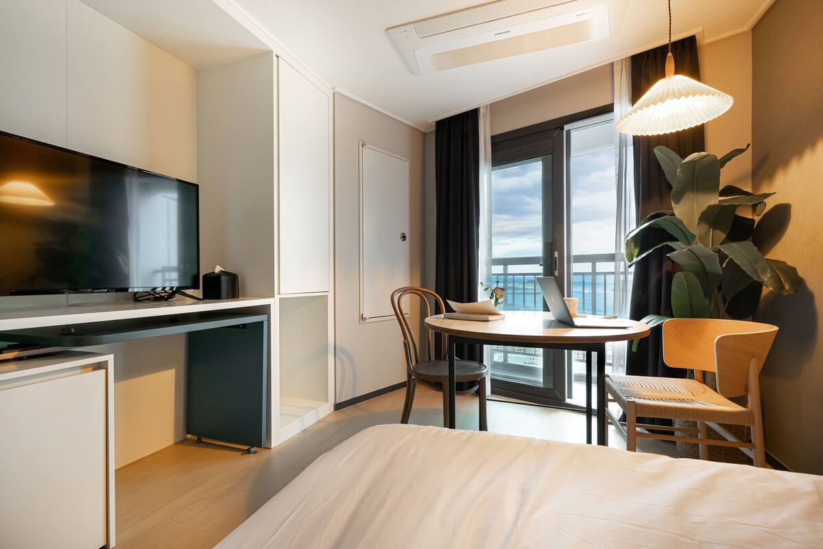 Ein Hotelzimmer mit einem Bett, einem Schreibtisch mit Laptop, einem Fernseher und einem großen Fenster mit Blick.