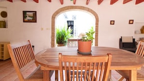 A wooden dining table with chairs, a potted plant, and a view through an arched doorway to an outdoor area with plants and a building.