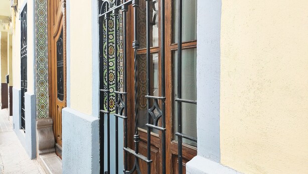 A narrow street with buildings featuring ornate metal gates and wooden doors.